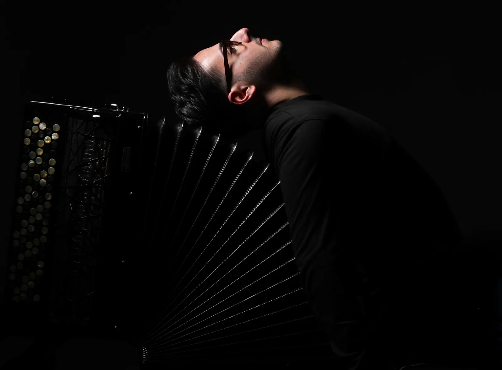 Luigi Gordano with his head resting back on the extended bellows, lit from one side