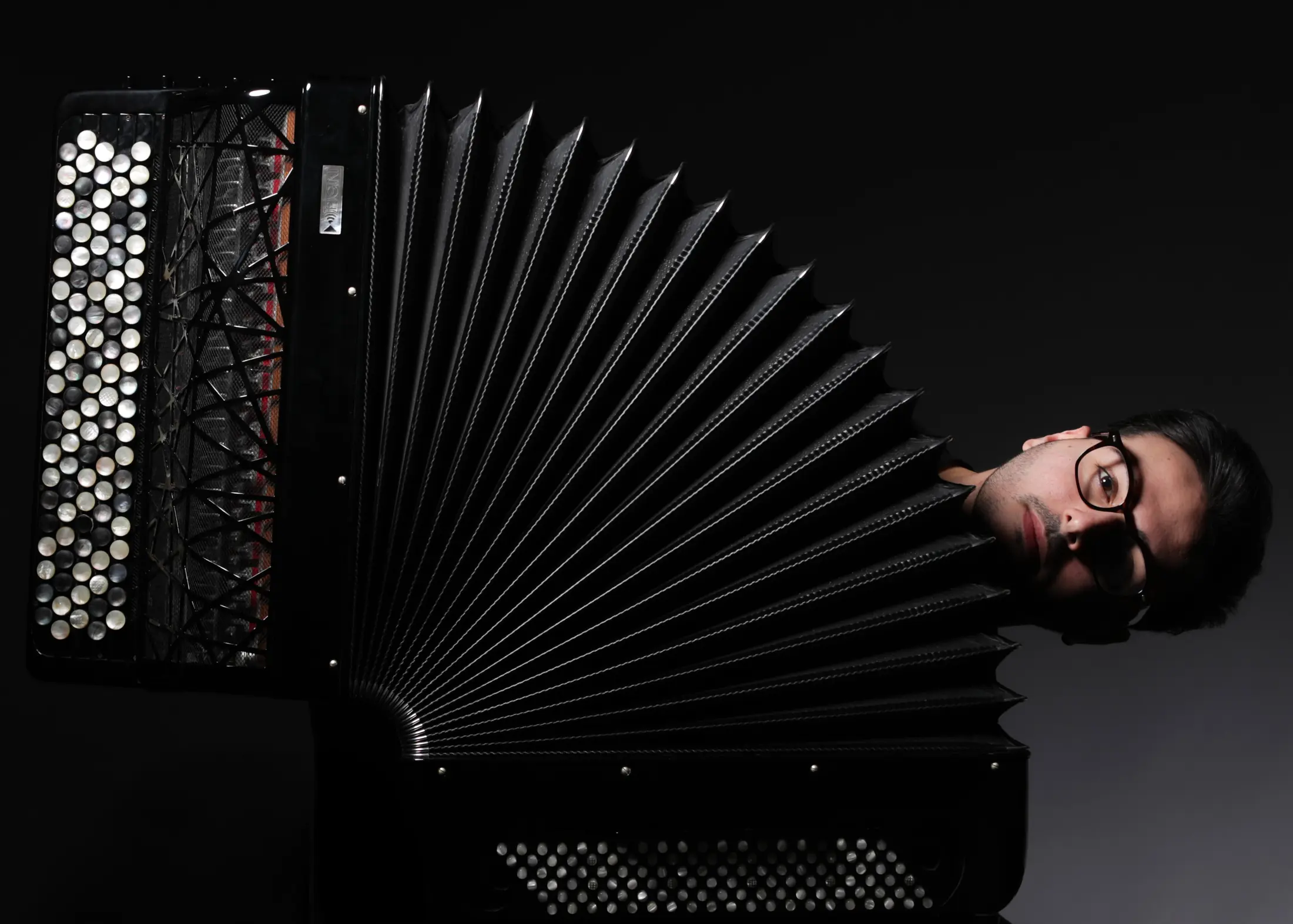 Luigi Gordano looking out from behind the open bellows of a concert accordion